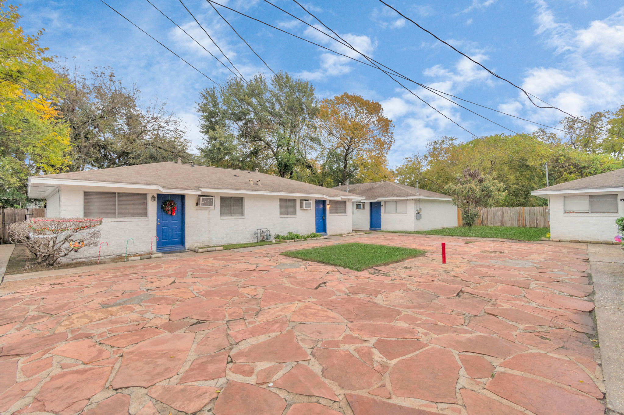 Cozy duplex with bright blue doors, stone-paved courtyard, and surrounded by greenery in a quiet residential area.